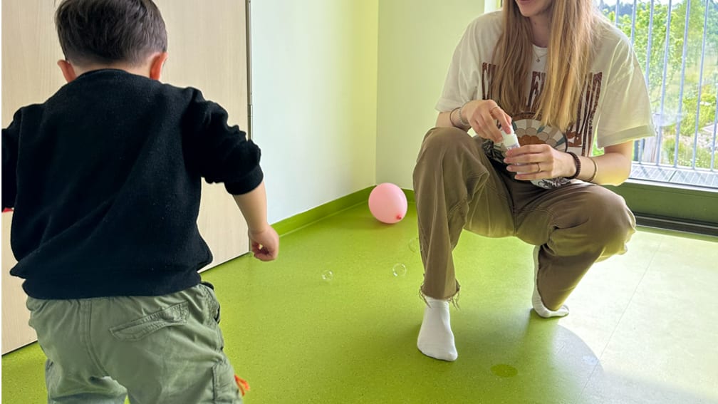 Betreuerin spielt mit einem Kind Ball