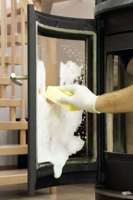 Lifestyle: Hand mit gelbem Handschuh reinigt Ofenscheibe mit schäumendem Reiniger