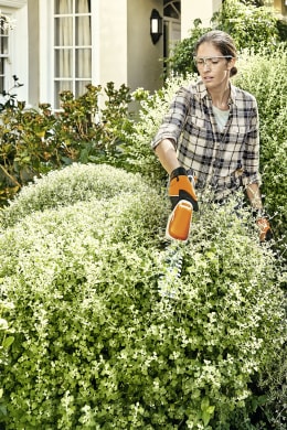 Lifestyle: Frau schneidet Buchsbaum im Garten mit STIHL Akku-Grasschere HSA 26