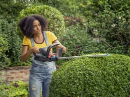Lifestyle: Frau schneidet Hecke mit GARDENA Akku-Heckenschere im Garten