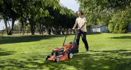 Lifestyle: Mann mäht Rasen mit Husqvarna® Benzin-Rasenmäher in sonnigem Garten