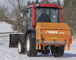Produktbild: RAUCH Winterdienststreuer UKS, orange, montiert an rotem Traktor im Wintereinsatz