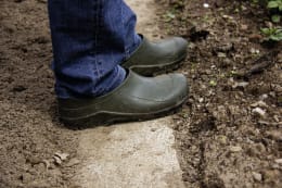 Lifestyle: Person trägt olivgrüne Gartenschuhe auf Erdboden im Garten