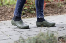 Lifestyle: Person trägt olivgrüne nora Gartenschuhe Comfy auf Steinweg im Garten