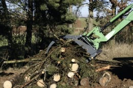 Produktbild: Heizomat® Greifzange an grünem Baggerarm beim Greifen von Stammholz und Strauchwerk