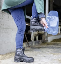 Lifestyle: Person zieht blauen Einmalüberschuh über Stiefel im Stallbereich