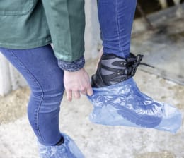 Lifestyle: Person trägt blaue Einmalüberschuhe über Schuhen im Außenbereich