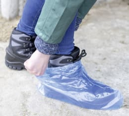 Lifestyle: Person zieht blauen Einmalüberschuh über Schuh an