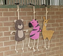 Lifestyle: Drei Pferdespielzeuge als Bär, Zebra und Lama mit Kordeln an Stallgitter aufgehängt