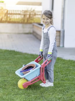 Lifestyle: Kind trägt bunte Handschuhe mit Traktor-Motiv beim Spielen mit Schubkarre im Garten