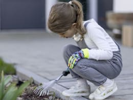 Lifestyle: Kind trägt Handschuhe mit Traktor-Motiv bei der Gartenarbeit
