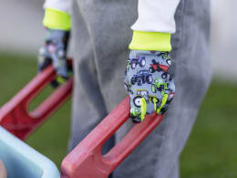 Lifestyle: Kind trägt Handschuhe mit buntem Traktor-Motiv beim Spielen auf einem Klettergerüst