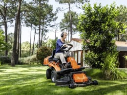 Produktbild: Husqvarna Rider R 214T Aufsitzmäher mit Mähdeck in orange, im Garten in Betrieb