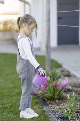 Lifestyle: Kind gießt Blumen im Garten mit Kinderhandschuhen mit Schmetterling-Motiv