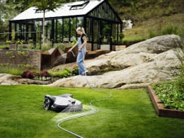 Lifestyle: Husqvarna® Mähroboter beim Mähen im Garten mit Person im Hintergrund