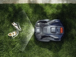 Lifestyle: Husqvarna® Mähroboter auf Rasen neben Rasensprenger in Vogelperspektive