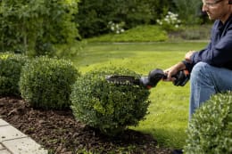 Lifestyle: Mann schneidet Buchsbaum mit Husqvarna® Akku-Grasschere Aspire® S20-P4A im Garten