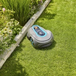 Produktbild: GARDENA Mähroboter smart SILENO free in grau mit türkisen Akzenten auf Rasen neben Blumenbeet