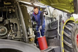 Produktbild: Fettpumpen-Set LubeDrive für Akkuschrauber im Einsatz an Landmaschine mit rotem Fetteimer