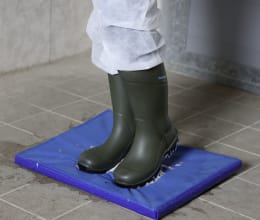 Lifestyle: Person in Gummistiefeln steht auf blauer Desinfektionsmatte zur Schuhdesinfektion