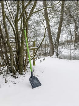 Lifestyle: Aluschaufel mit Holzstiel steht im Schnee vor winterlicher Waldkulisse