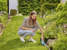 Lifestyle: Frau schneidet Rasenkante mit GARDENA Akku-Grasschere PowerCut 20 im Garten