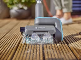 Produktbild: GARDENA Akku-Multi-Reiniger AquaBrush mit Bürste und Wasserdüsen auf Holzterrasse