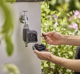 Lifestyle: Person wechselt Batterie am GARDENA Bewässerungscomputer smart Water Control an Außenwasserhahn