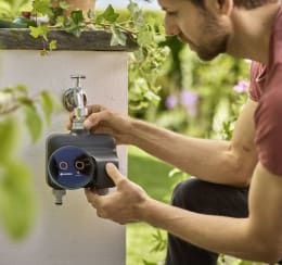 Lifestyle: Mann bedient GARDENA Bewässerungscomputer smart Dual Water Control an Außenwasserhahn im Garten