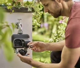 Lifestyle: Mann bedient GARDENA Bewässerungscomputer smart Dual Water Control am Wasserhahn im Garten