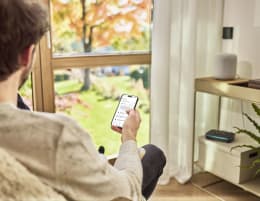 Lifestyle: Person steuert GARDENA Bewässerungscomputer per Smartphone-App am Fenster mit Gartenblick