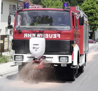 Produktbild: LEHNER® Ölbinderstreuer Öl Tiger® montiert an Feuerwehrfahrzeug beim Streuen von Ölbindemittel