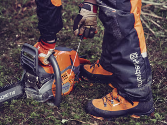 Lifestyle: Person mit Husqvarna® Benzin-Kettensäge bei der Waldarbeit mit Schutzkleidung und Handschuhen