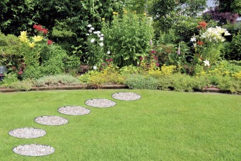 Lifestyle: Runde Rasenkanten aus Stahlblech mit Kiesfüllung im Rasen vor buntem Blumenbeet