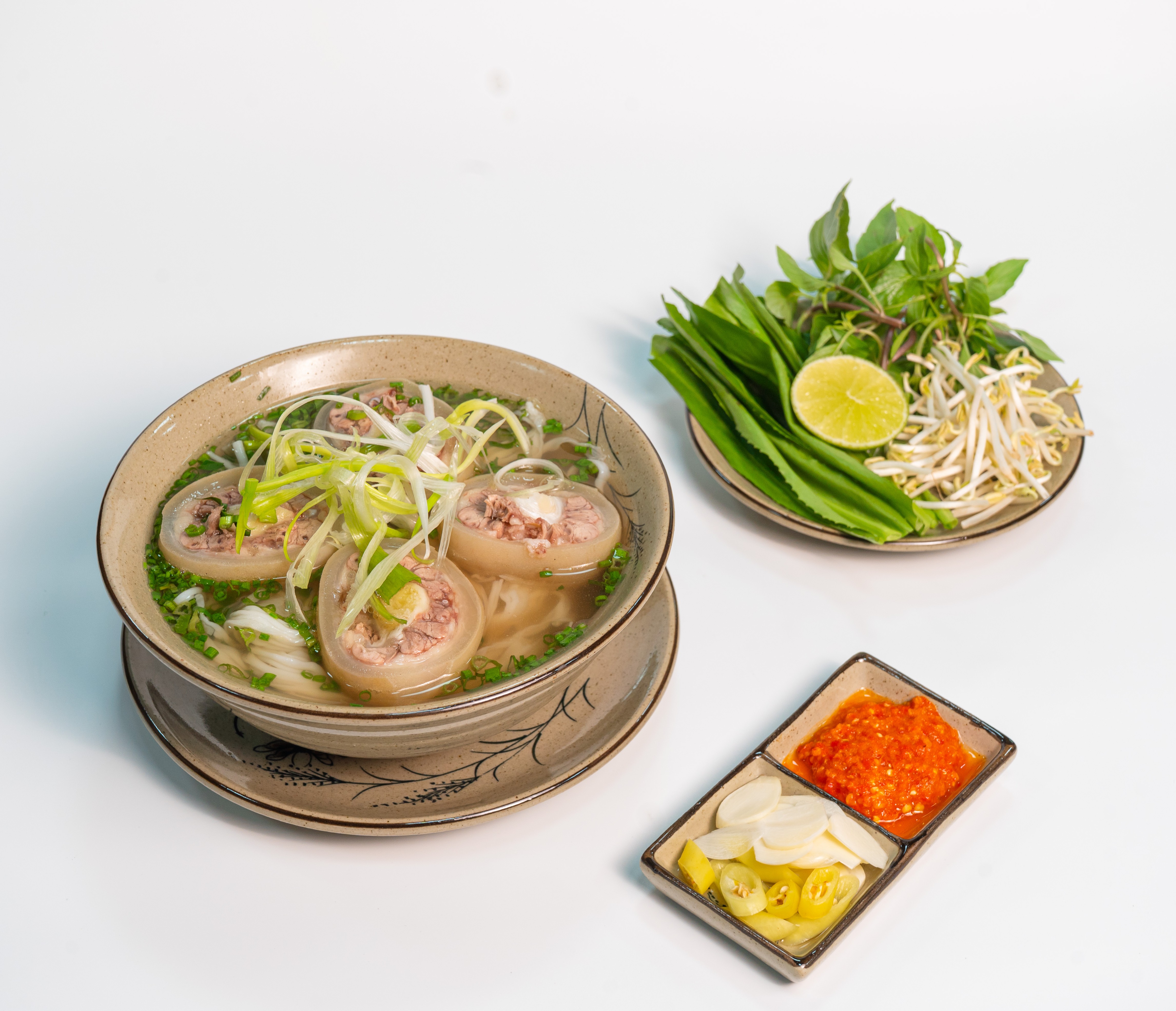 一碗牛尾河粉,牛尾段铺在米粉上,旁边摆放着一盘生菜和豆芽