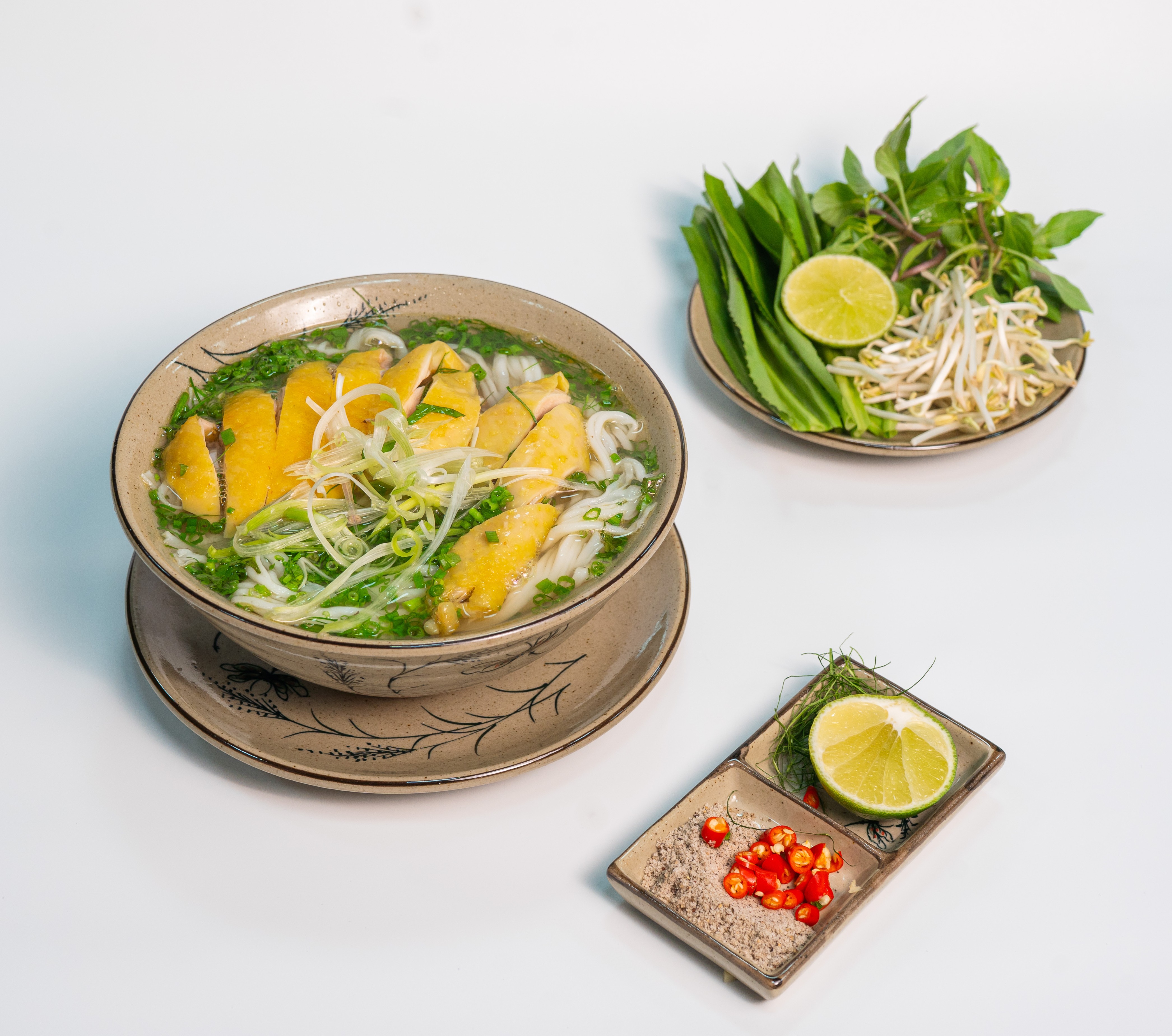 一碗鸡肉河粉,配有金黄色鸡皮、葱花和一碟豆芽、柠檬、辣椒
