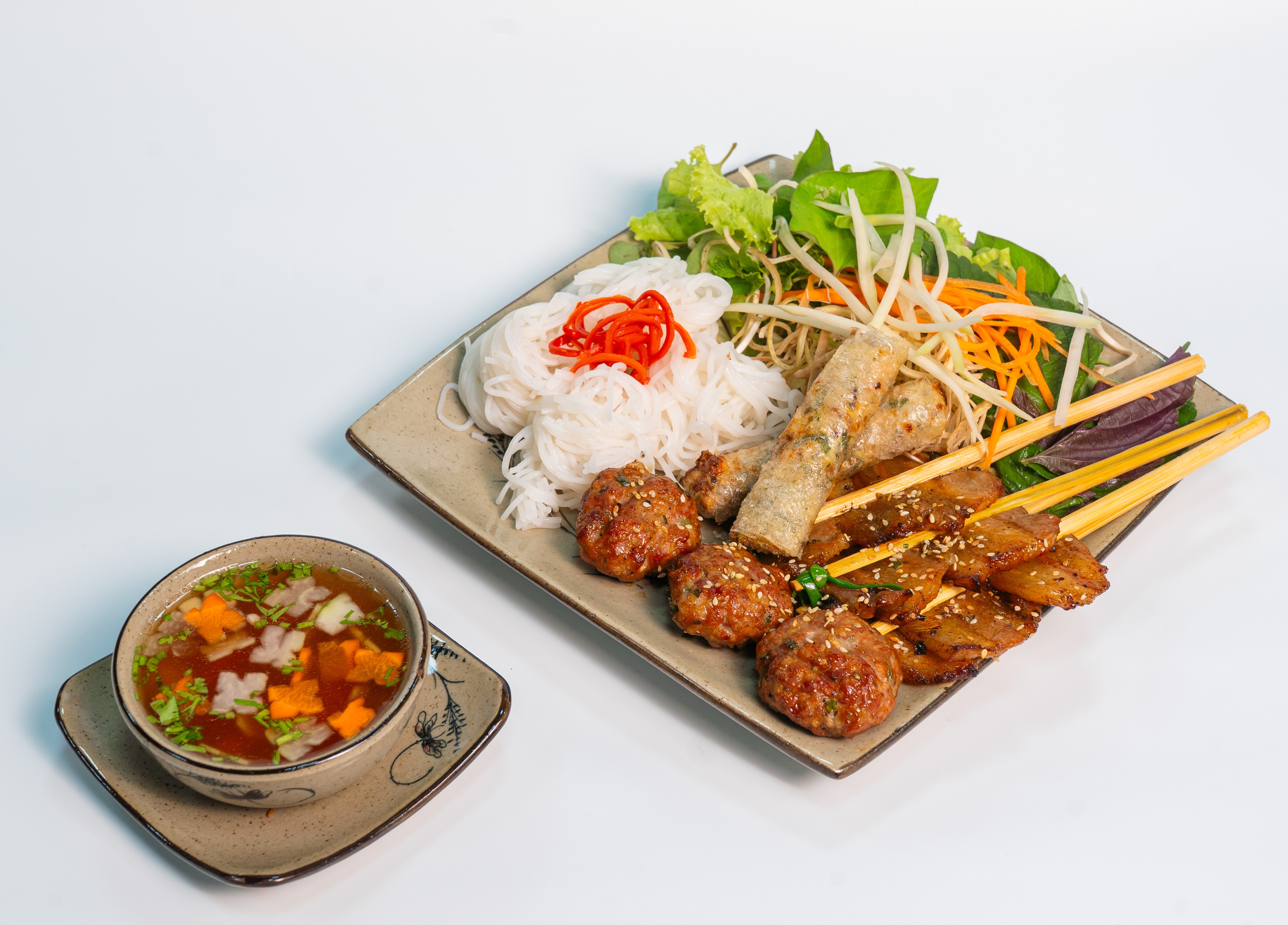 一盘烤肉米线,配有肉丸、烤肉片、米线、生菜和一碗蘸酱