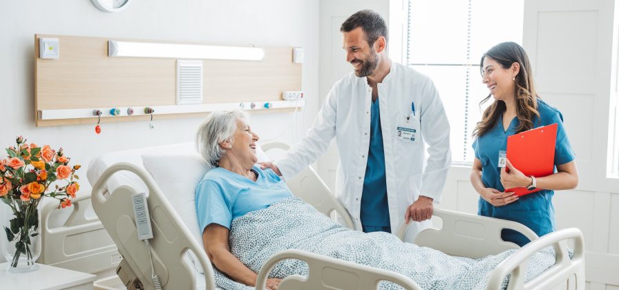 A doctor and nurse review post-procedure care with a patient seated in a hospital bed