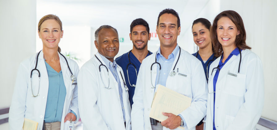 A group of doctors and nurses smile toward the camera in a hallway
