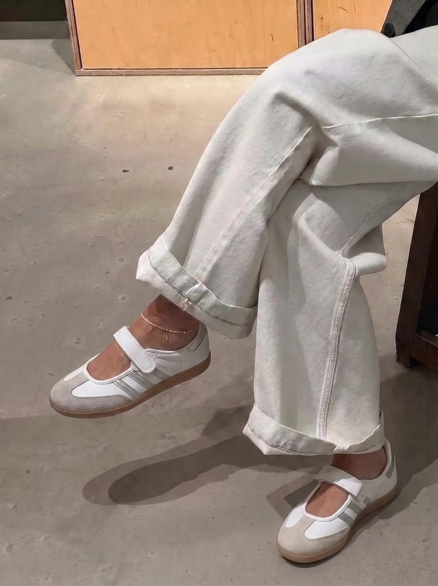 Woman wearing white and grey adidas Samba Jane Mary Jane sneakers with cuffed white trousers, indoor store setting