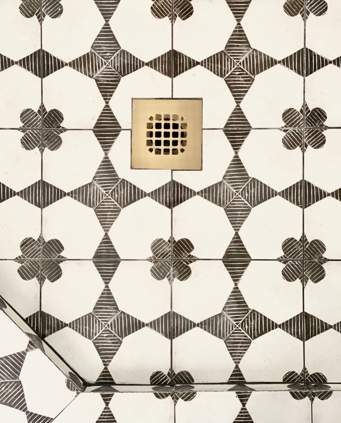 View of the shower drain tiled in Enchante 8x8 porcelain tile in Moderno