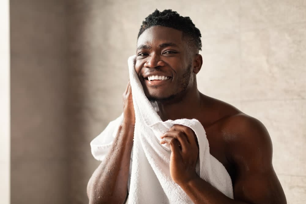 A imagem mostra um homem sorrindo enquanto seca a barba