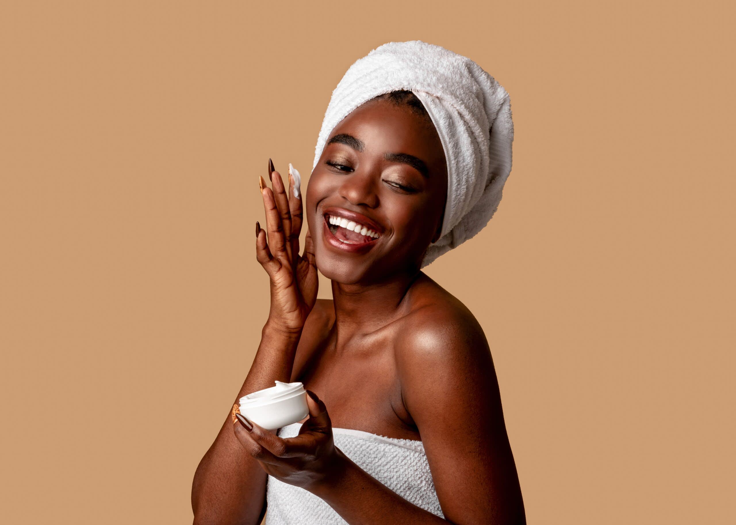 Imagem de mulher sorrindo enquanto aplica creme no rosto