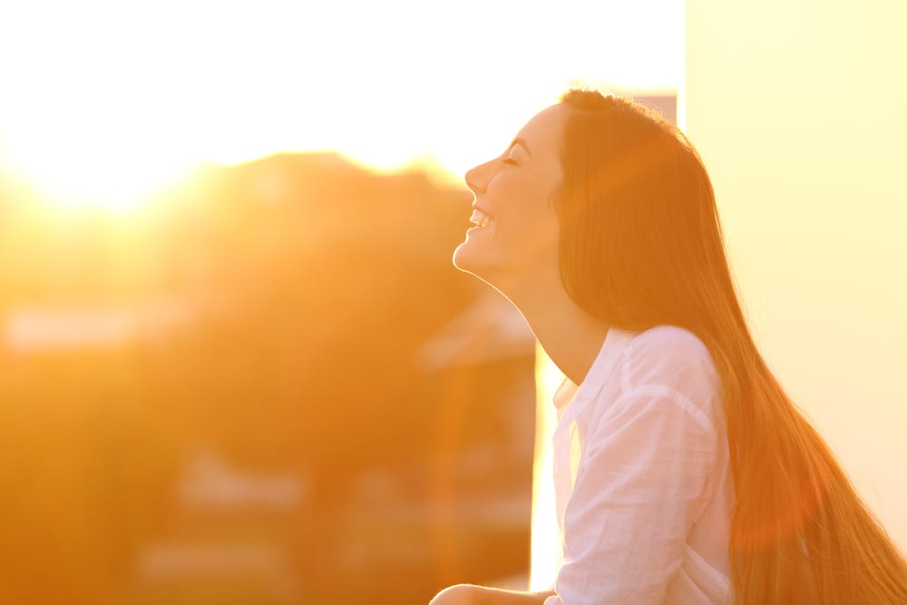 Imagem de mulher sorridente, ao fundo está o por do sol