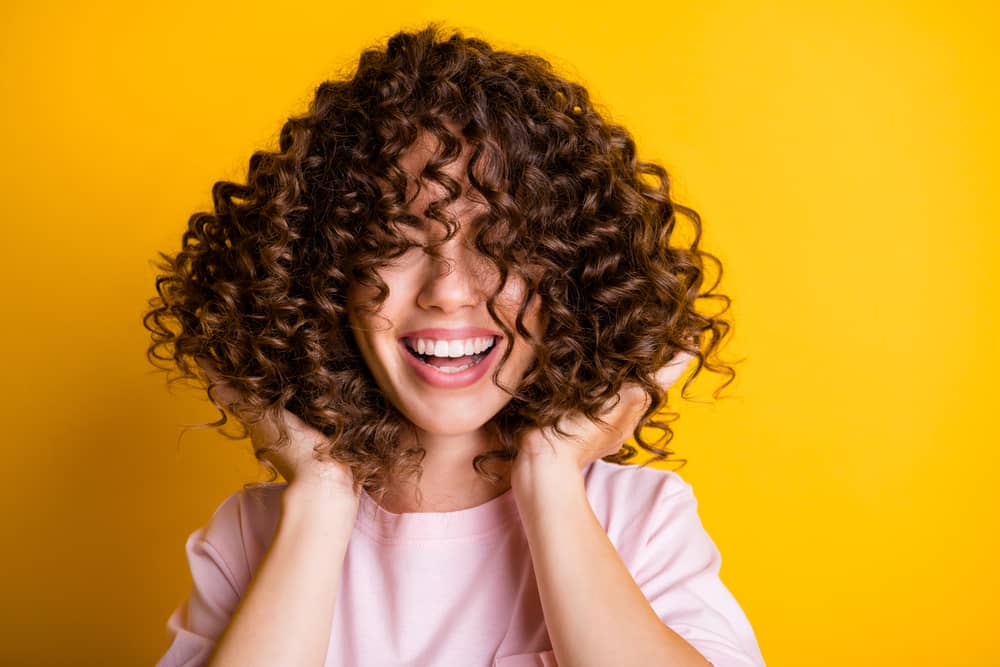 Imagem de mulher sorridente brincando com o cabelo cacheado