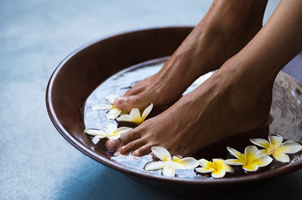 Imagem de pés mergulhados em um recipiente com água e flores
