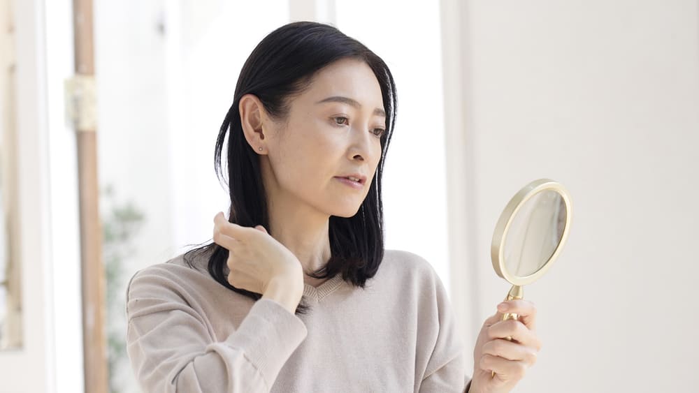 A imagem mostra uma mulher tocando o próprio cabelo enquanto se olha no espelho