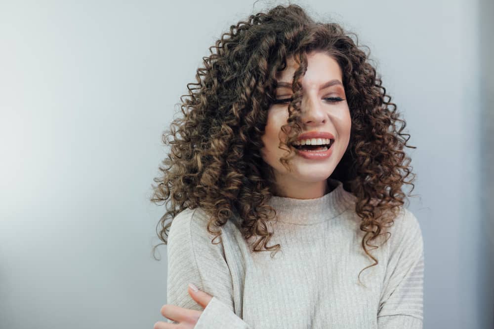 A imagem mostra uma mulher sorrindo, ela tem cabelo cacheado e está usando um agasalho para o frio