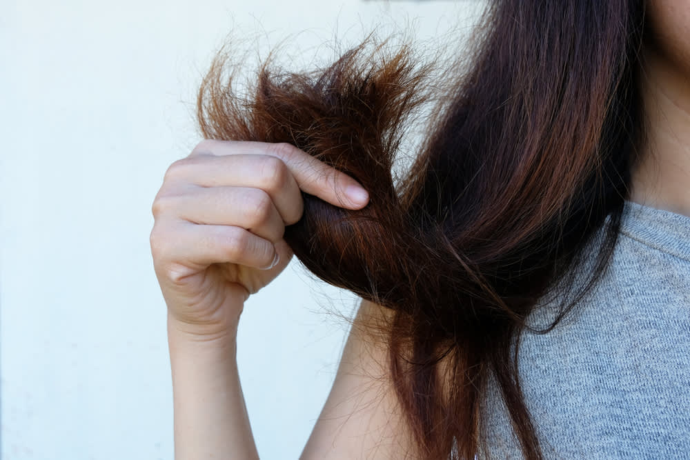 Imagem de mulher mostrando as pontas do seu cabelo que está ressecada e quebrada