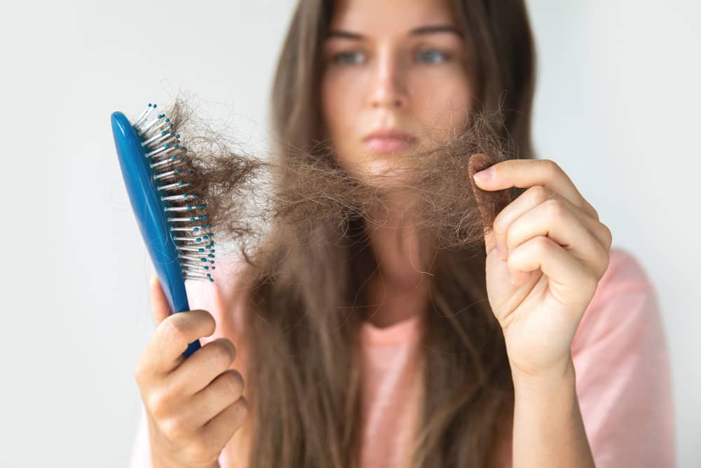 Imagem de mulher olhando para cabelo quebrado na escova de cabelo